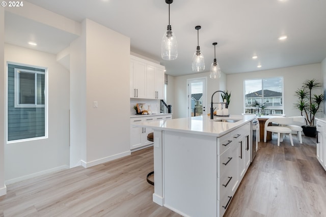 kitchen featuring sink, light hardwood / wood-style flooring, an island with sink, white cabinets, and decorative light fixtures