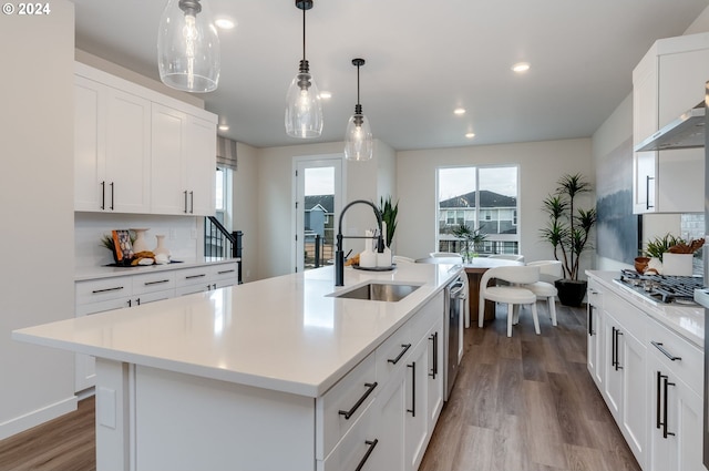 kitchen featuring appliances with stainless steel finishes, sink, white cabinets, hanging light fixtures, and a center island with sink