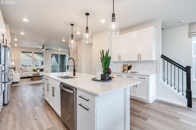 kitchen featuring appliances with stainless steel finishes, white cabinetry, sink, hanging light fixtures, and a center island with sink