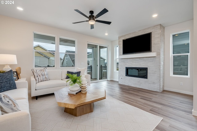 living room featuring ceiling fan, a large fireplace, and light hardwood / wood-style flooring