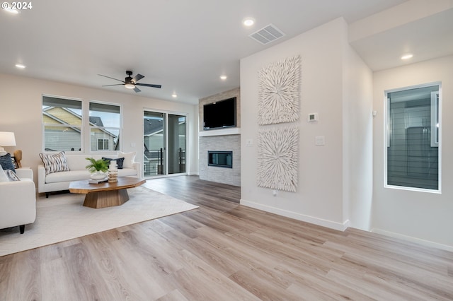 living room with a stone fireplace, light hardwood / wood-style floors, and ceiling fan