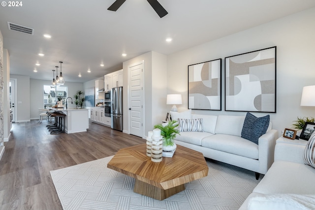 living room featuring ceiling fan, sink, and light wood-type flooring