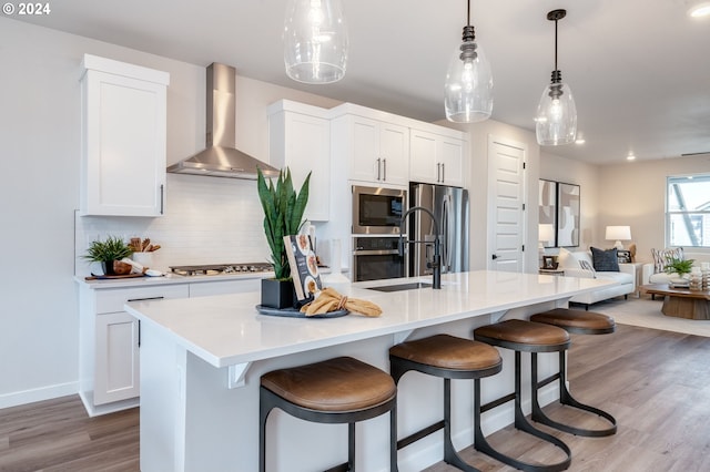 kitchen featuring white cabinetry, a kitchen island with sink, and wall chimney range hood