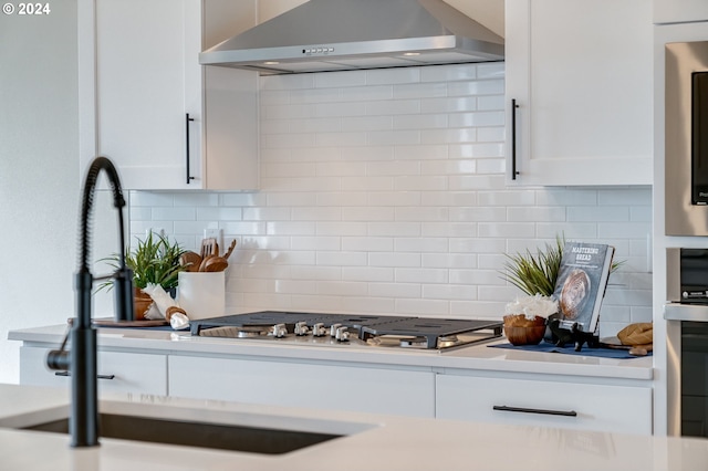 kitchen featuring tasteful backsplash, white cabinets, stainless steel appliances, and wall chimney exhaust hood