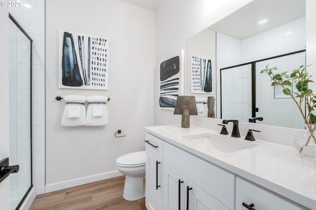 bathroom featuring wood-type flooring, toilet, a shower with shower door, and vanity