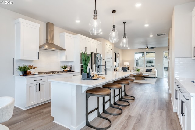 kitchen with white cabinetry, an island with sink, pendant lighting, and wall chimney exhaust hood