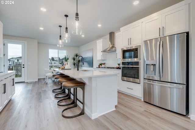 kitchen featuring appliances with stainless steel finishes, pendant lighting, an island with sink, sink, and wall chimney exhaust hood