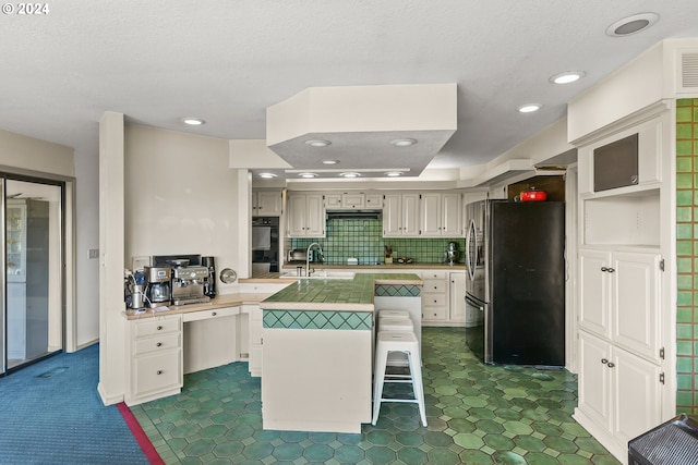 kitchen with tasteful backsplash, a kitchen bar, a kitchen island with sink, white cabinetry, and stainless steel refrigerator