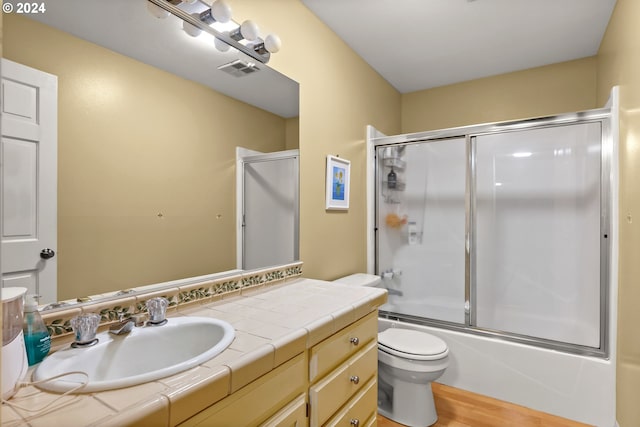 full bathroom featuring oversized vanity, hardwood / wood-style flooring, combined bath / shower with glass door, and toilet