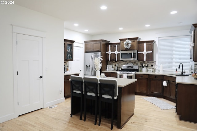 kitchen with sink, stainless steel appliances, light hardwood / wood-style floors, a breakfast bar, and a kitchen island