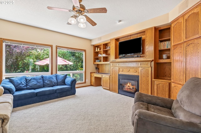 living room with light carpet, a ceiling fan, a textured ceiling, and a glass covered fireplace