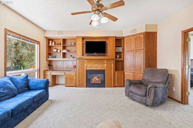 living area featuring light carpet, a ceiling fan, a glass covered fireplace, and a textured ceiling
