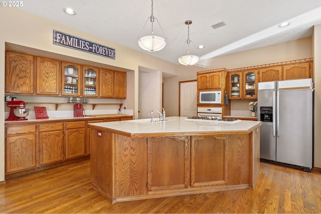 kitchen featuring stainless steel fridge, white microwave, a sink, light countertops, and brown cabinets