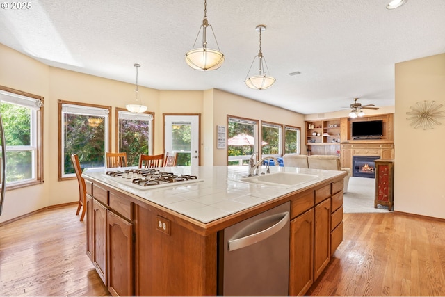 kitchen with white gas stovetop, stainless steel dishwasher, a sink, a glass covered fireplace, and tile counters
