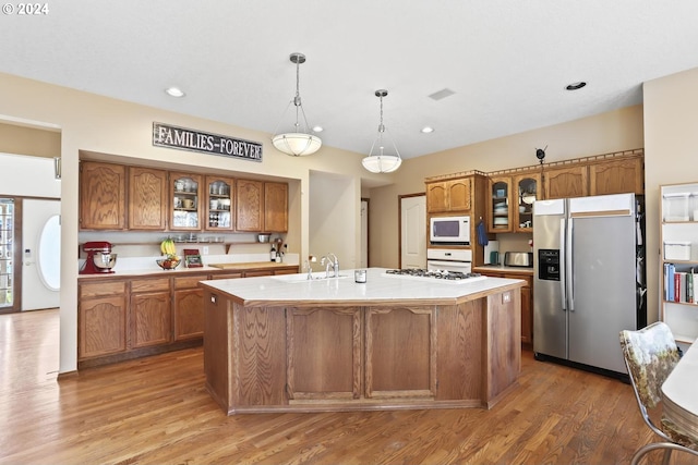 kitchen with pendant lighting, hardwood / wood-style floors, white microwave, a center island with sink, and stainless steel refrigerator with ice dispenser