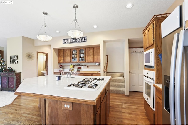 kitchen with white appliances, sink, wood-type flooring, pendant lighting, and an island with sink