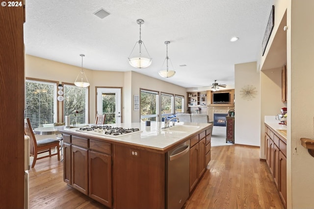 kitchen with dishwasher, white gas cooktop, a kitchen island with sink, sink, and decorative light fixtures