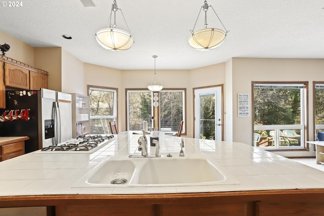 kitchen featuring white gas cooktop, sink, pendant lighting, stainless steel fridge with ice dispenser, and tile counters