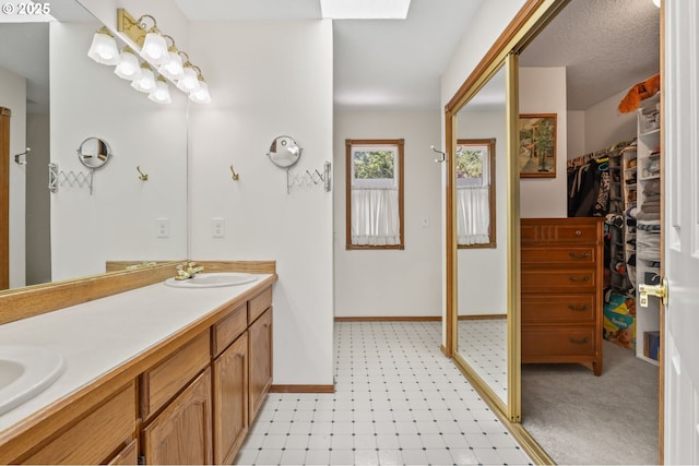 full bath featuring baseboards, double vanity, and a walk in closet