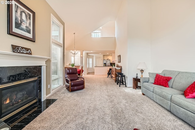 carpeted living area with a chandelier, a high end fireplace, a towering ceiling, and baseboards