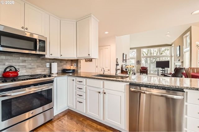 kitchen with light stone counters, stainless steel appliances, tasteful backsplash, white cabinetry, and a sink