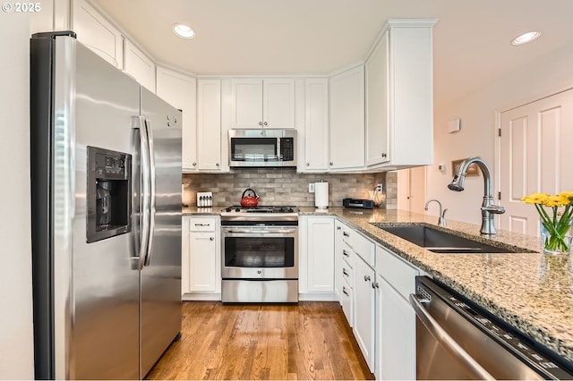 kitchen featuring a sink, white cabinetry, light wood-style floors, appliances with stainless steel finishes, and backsplash