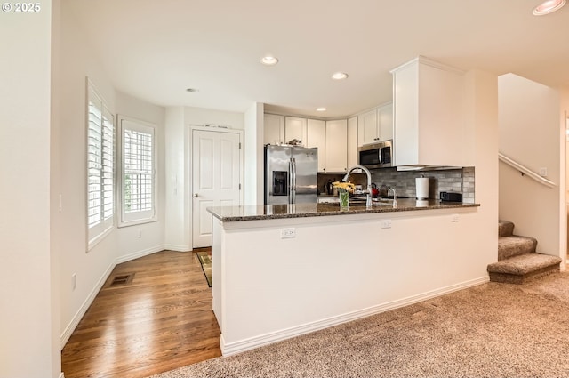 kitchen featuring stainless steel appliances, decorative backsplash, white cabinets, dark stone countertops, and a peninsula