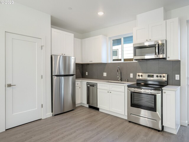 kitchen with appliances with stainless steel finishes, tasteful backsplash, white cabinets, and light hardwood / wood-style floors