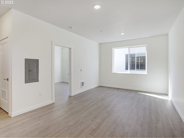 empty room with light wood-style floors, baseboards, electric panel, and visible vents