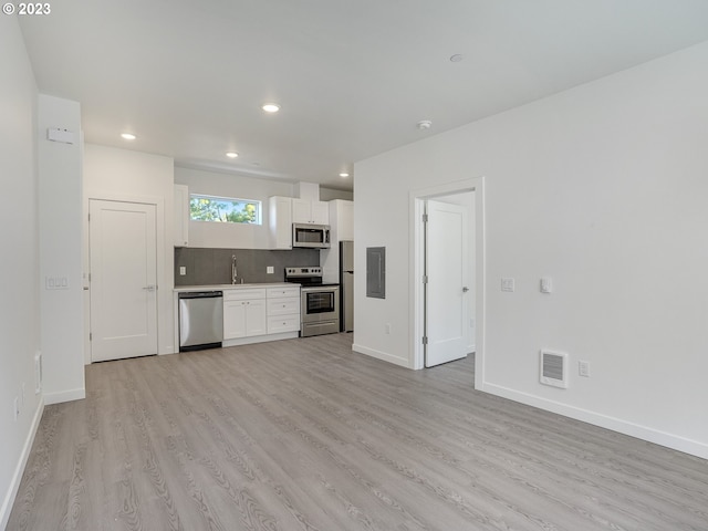 kitchen with white cabinets, backsplash, light wood-type flooring, stainless steel appliances, and sink