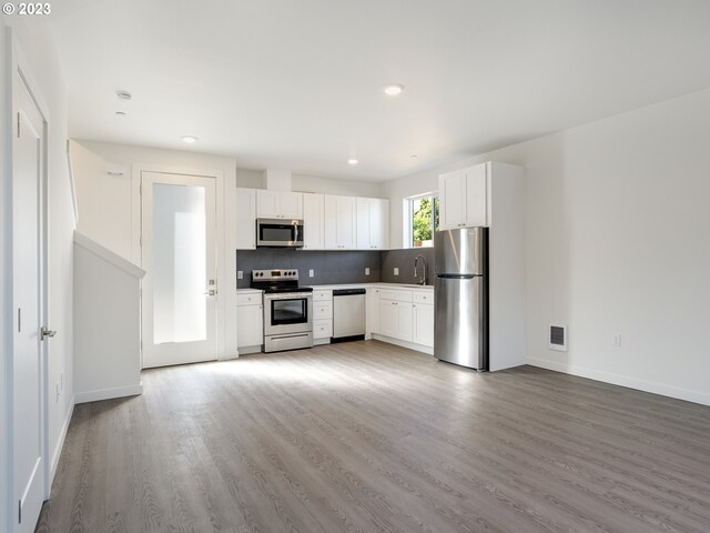 kitchen with appliances with stainless steel finishes, white cabinetry, wood-type flooring, and backsplash