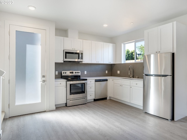 kitchen featuring stainless steel appliances, a sink, white cabinets, light countertops, and backsplash