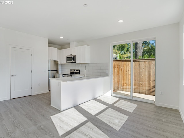 kitchen with light hardwood / wood-style flooring, appliances with stainless steel finishes, white cabinetry, and decorative backsplash