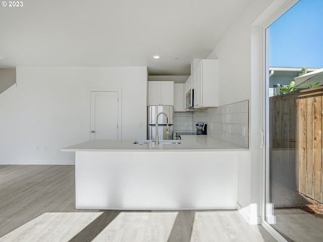 kitchen featuring light hardwood / wood-style floors, kitchen peninsula, stainless steel appliances, decorative backsplash, and white cabinetry