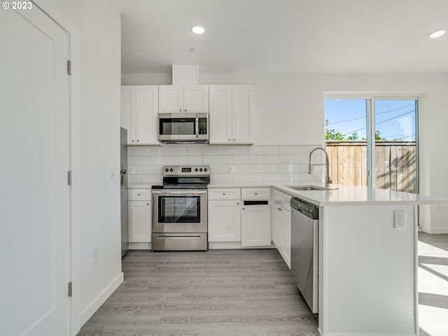 kitchen with kitchen peninsula, sink, appliances with stainless steel finishes, and light hardwood / wood-style floors