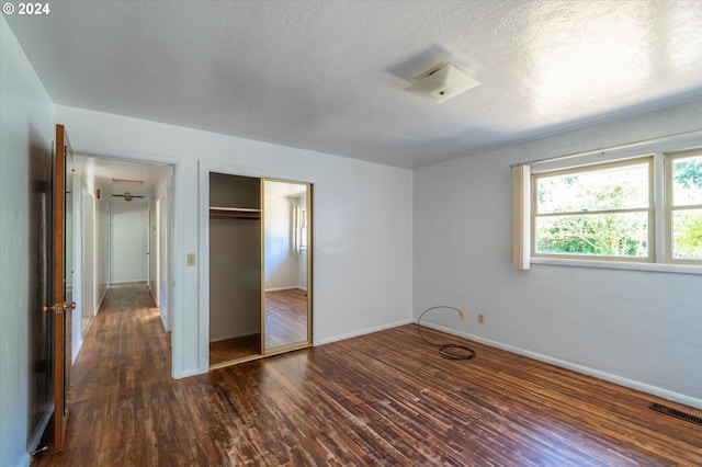 unfurnished bedroom featuring a textured ceiling, dark hardwood / wood-style floors, and a closet