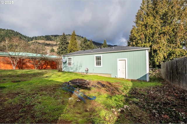 rear view of property featuring a mountain view, a yard, and a fire pit