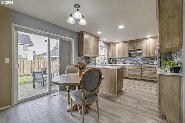 kitchen with hanging light fixtures, gas stovetop, light wood-type flooring, and decorative backsplash