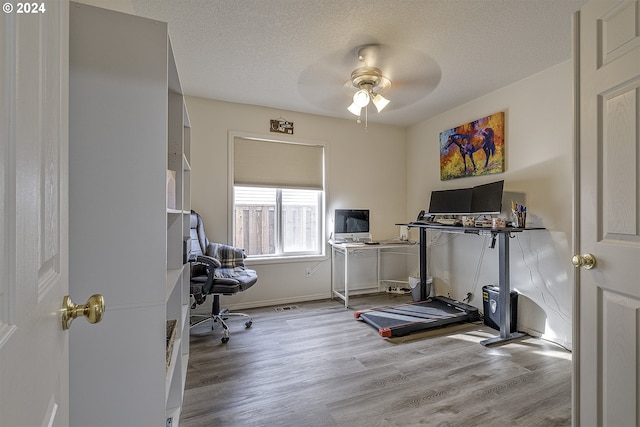 exercise area featuring a textured ceiling, light hardwood / wood-style floors, and ceiling fan