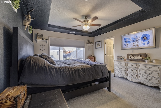 carpeted bedroom with a textured ceiling, ceiling fan, and a tray ceiling