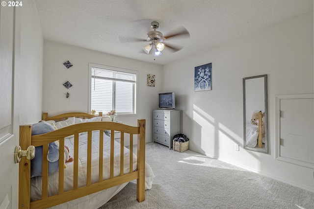 bedroom featuring a textured ceiling, carpet, ceiling fan, and a crib