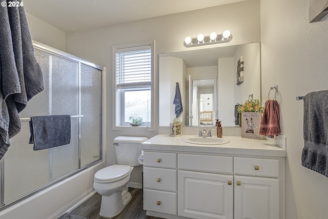 full bathroom featuring toilet, a textured ceiling, hardwood / wood-style flooring, combined bath / shower with glass door, and vanity