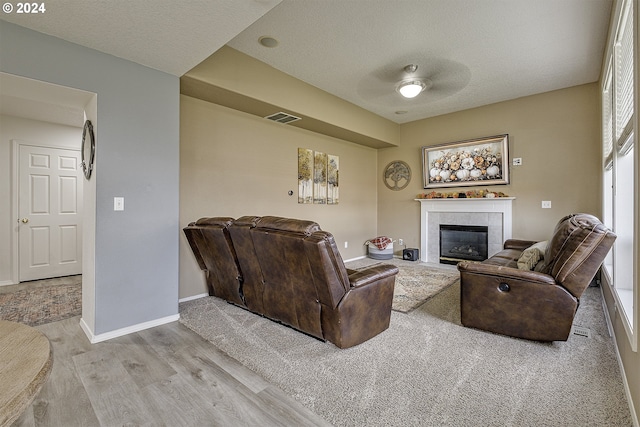 living room featuring a textured ceiling, a tile fireplace, ceiling fan, and light hardwood / wood-style flooring