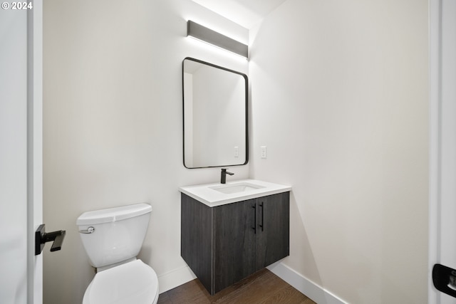 half bathroom with toilet, baseboards, wood finished floors, and vanity