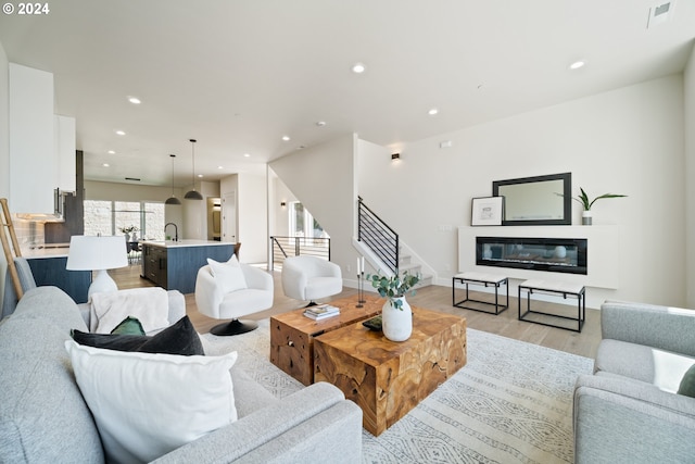 living area featuring recessed lighting, visible vents, stairs, light wood-type flooring, and a glass covered fireplace