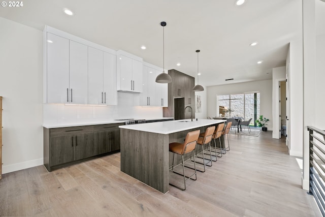 kitchen featuring a breakfast bar, light countertops, tasteful backsplash, modern cabinets, and a center island with sink