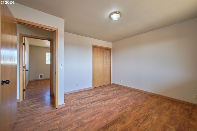 unfurnished bedroom with dark wood-type flooring, a closet, visible vents, and baseboards