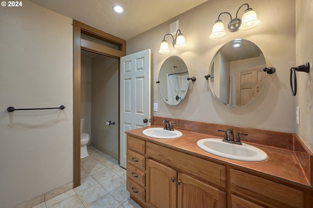 bathroom with double vanity, a sink, toilet, and tile patterned floors