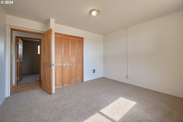 unfurnished bedroom featuring carpet, a textured ceiling, visible vents, and a closet