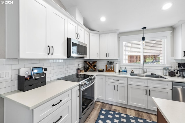 kitchen featuring sink, light hardwood / wood-style floors, pendant lighting, white cabinetry, and appliances with stainless steel finishes